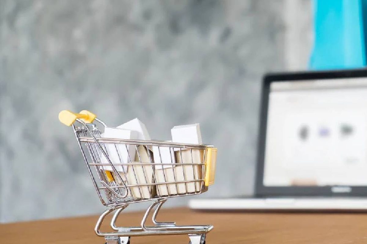 Miniature shopping cart filled with parcels beside a laptop