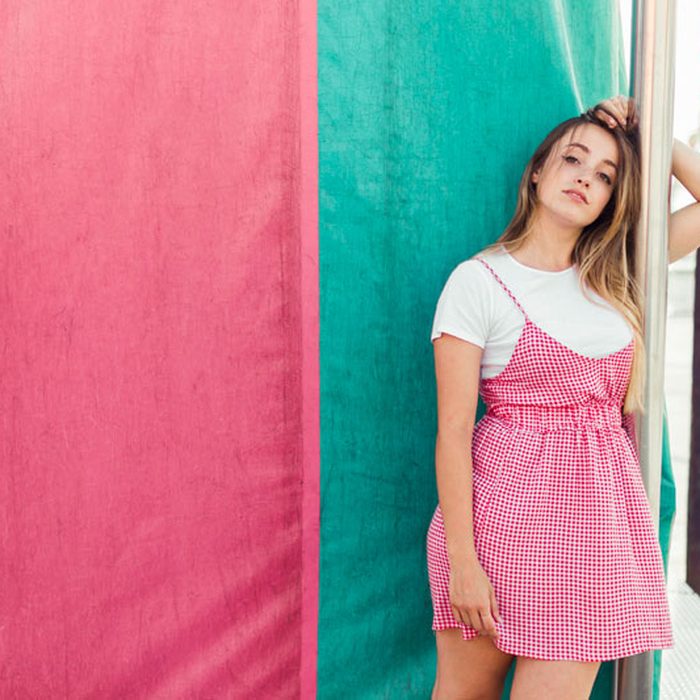 Shopper in a pink dress leaning on a colorful storefront wall